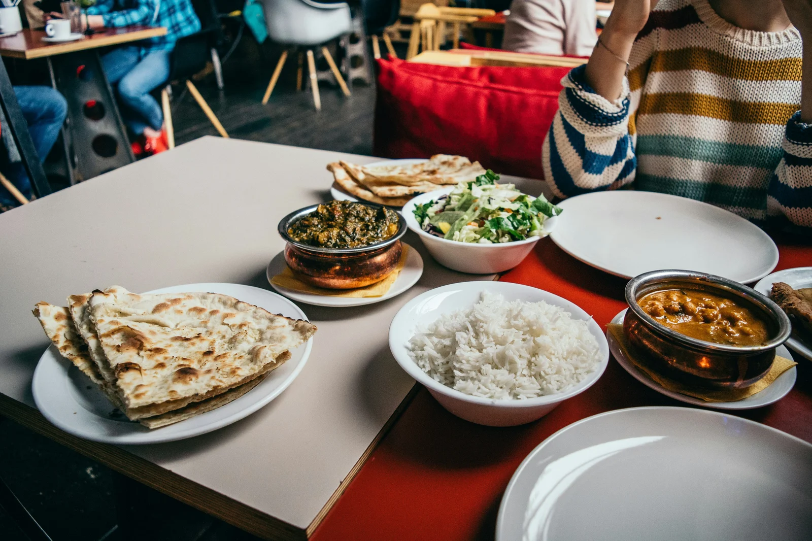 An Indian shared meal spread on a restaurant table with naan, curry, rice, and salad