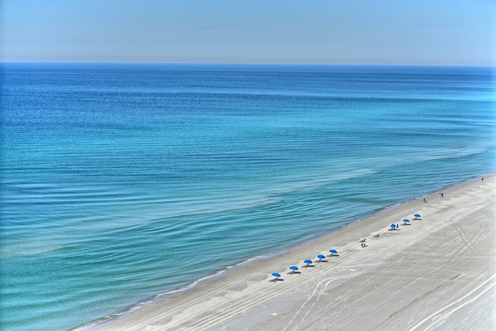 Quiet white sand Gulf Coast beach with turquoise water and a handful of beach umbrellas on a calm winter day