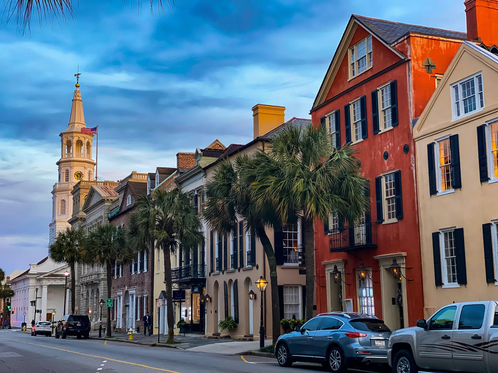 Historic Charleston streetscape at dusk with St. Michael's Church steeple, palm trees, and antebellum buildings along the peninsula