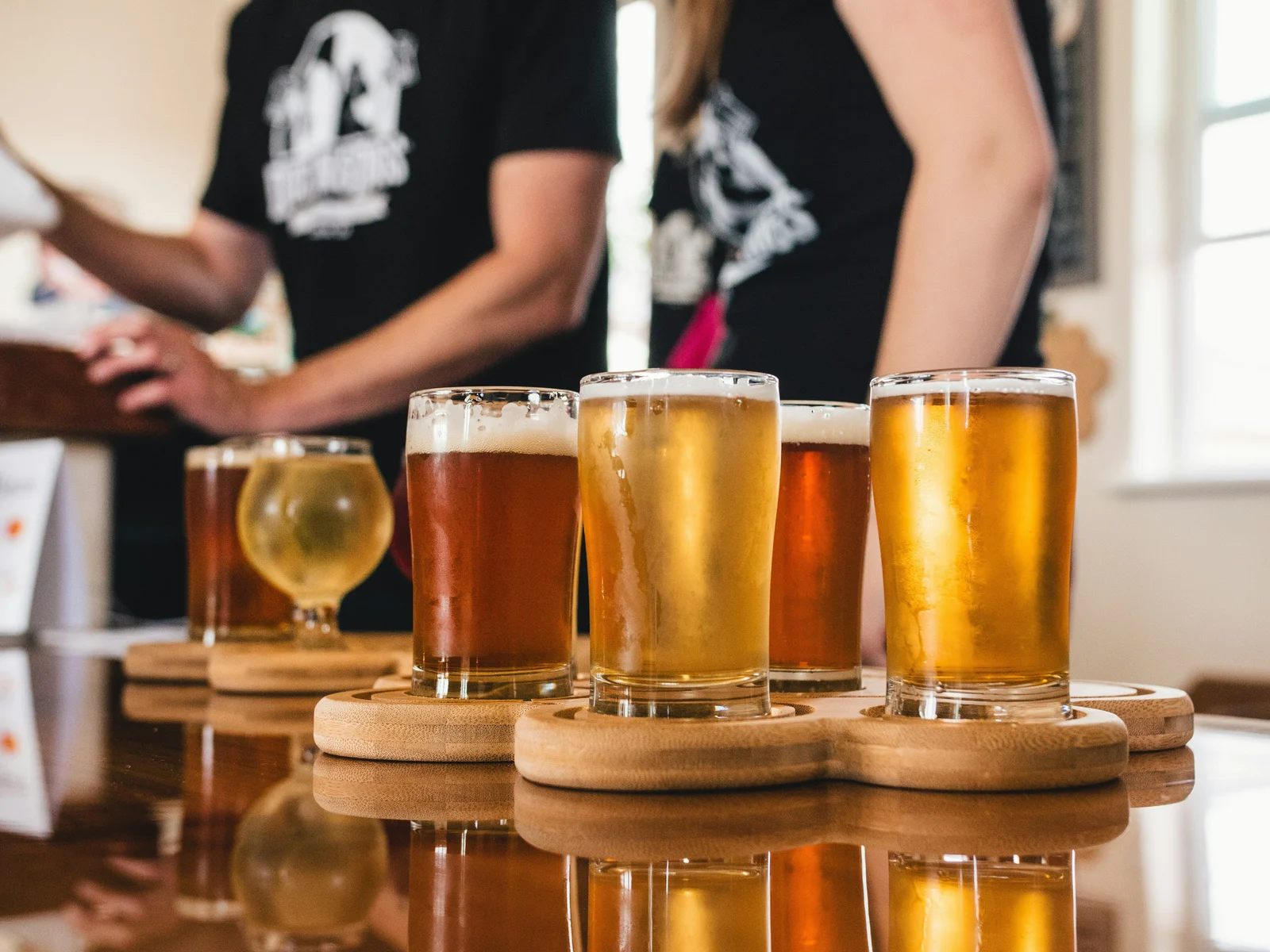 A wooden tasting board with four glasses of craft beer in varying shades from pale gold to amber