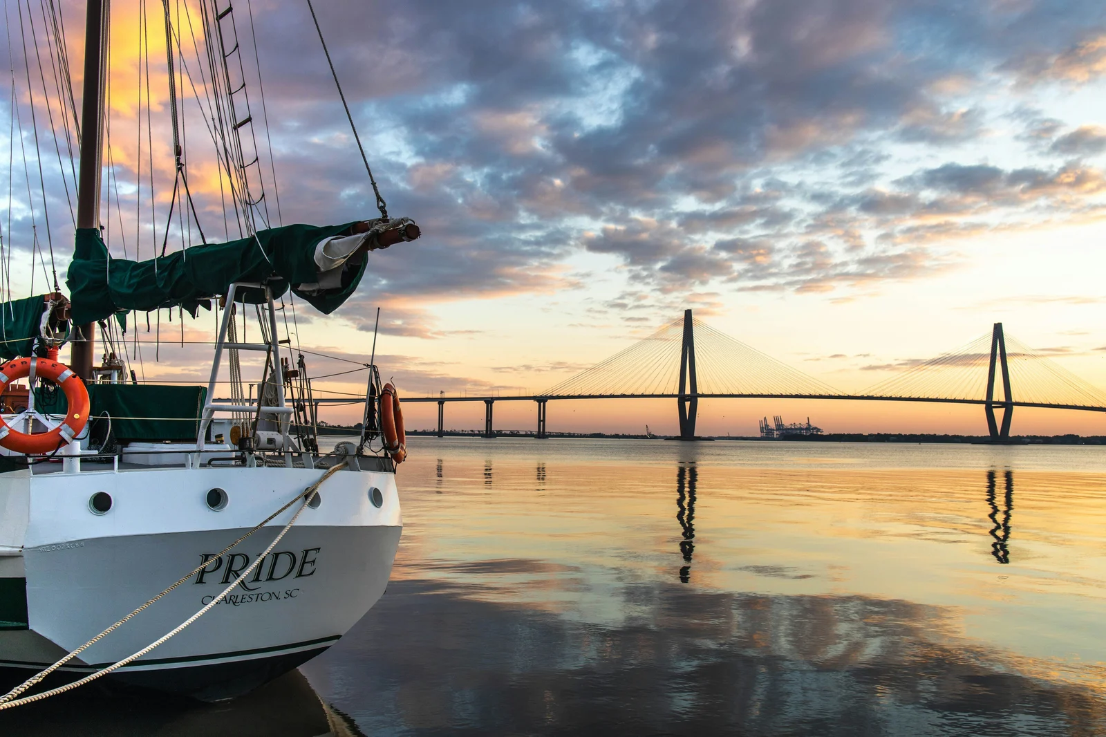 Sailboat moored at the Charleston waterfront at golden hour with the Arthur Ravenel Jr. Bridge in the background