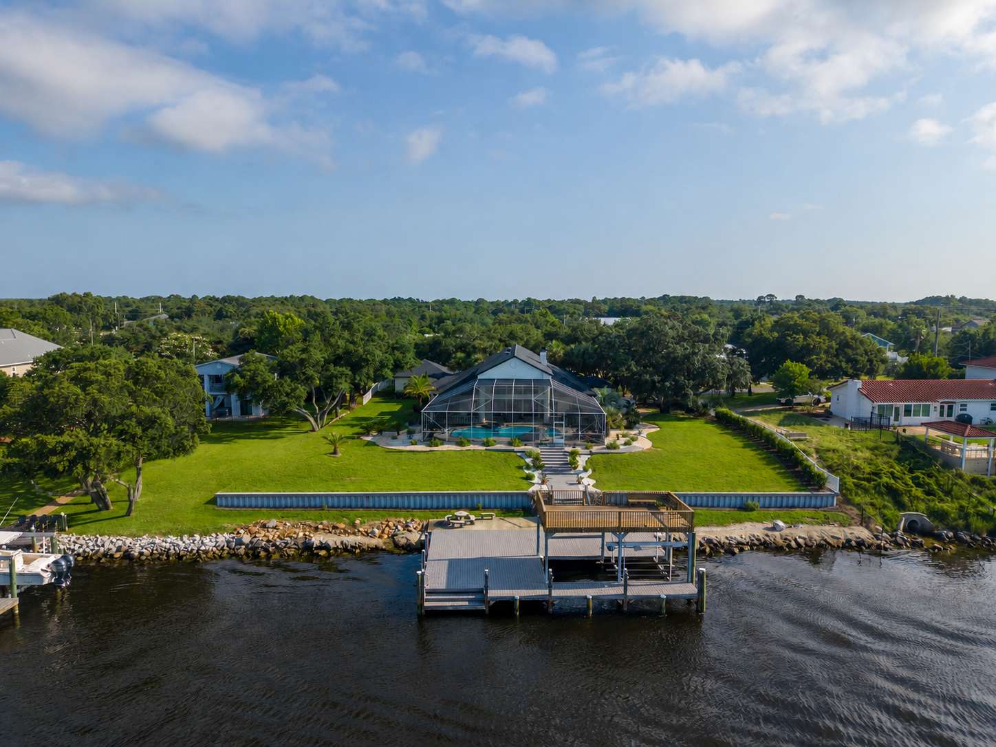 Aerial view of a waterfront LunaSol vacation rental with pool enclosure, dock and grounds on the Pensacola area coast