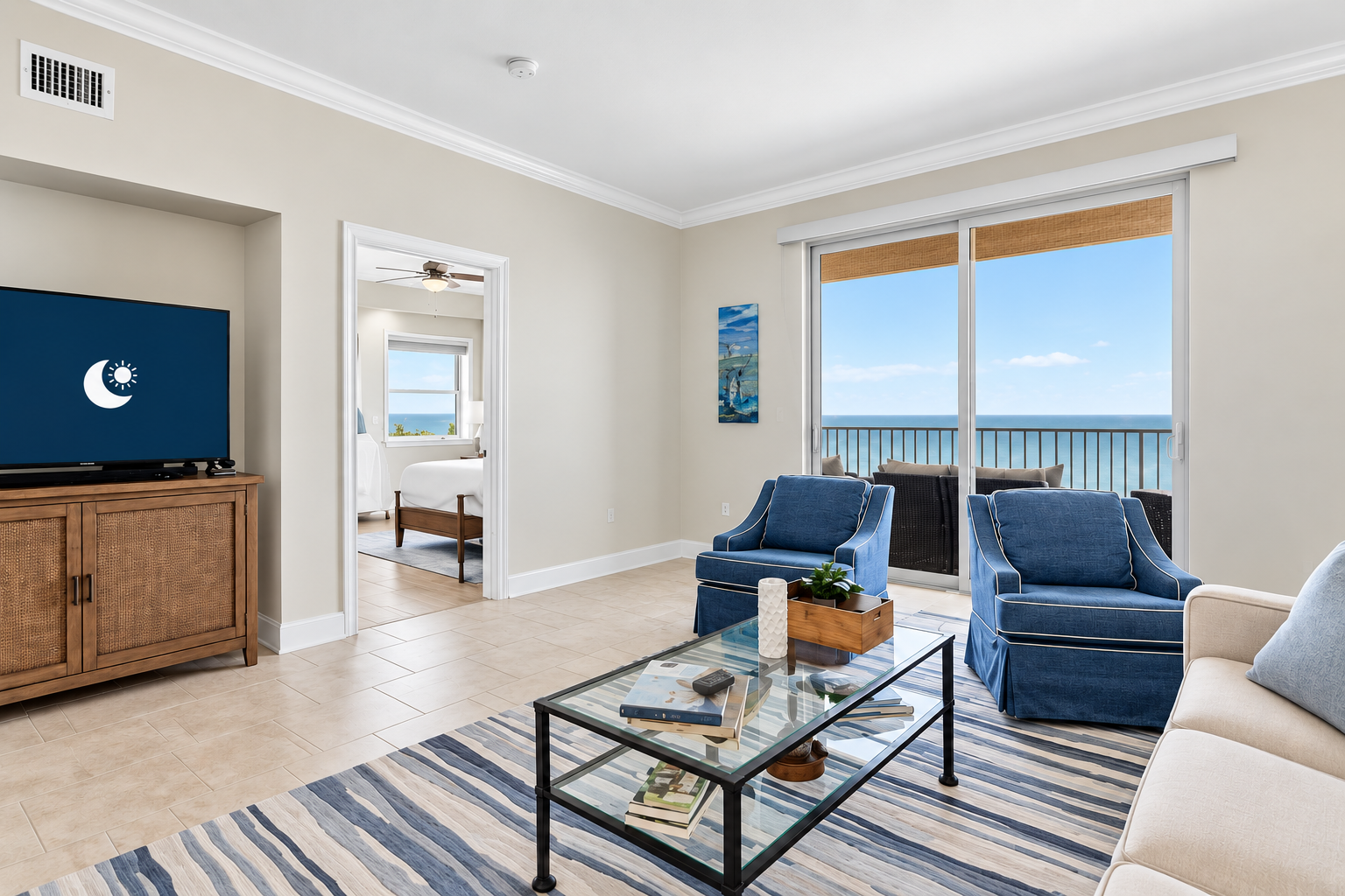 Harbour Pointe 301 living room — two navy upholstered armchairs, glass coffee table, warm neutral walls, and a wide sliding door opening onto the Gulf