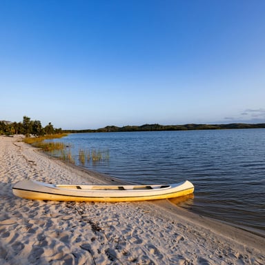 Canoe resting on white sand beside calm coastal water
