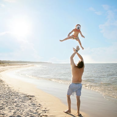 Father tossing child on a sunny white sand beach